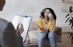 Young African American woman crying on session with psychologist, speaking to mental health professional at office