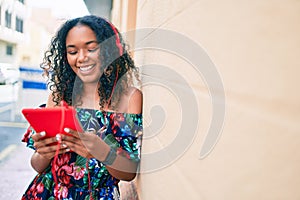 Young african american woman with curly hair smiling happy outdoors wearing headphones using touchpad