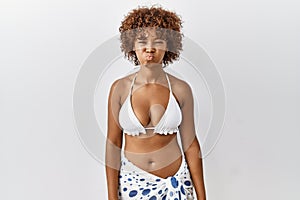 Young african american woman with curly hair wearing bikini puffing cheeks with funny face