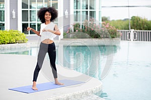 Young African American woman doing exercise with stretch muscles hands in the poolside.