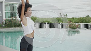 Young African American woman doing exercise with stretch muscles hands in the poolside.