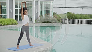 Young African American woman doing exercise with stretch muscles hands in the poolside.