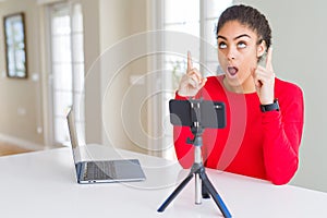 Young african american woman doing video call using smartphone camera amazed and surprised looking up and pointing with fingers