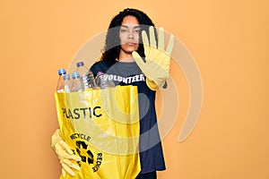 Young african american woman doing volunteering recycling holding bag with plastic bottles with open hand doing stop sign with