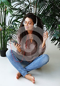 Young African American woman dressed casual listen to music and sitting on the floor at home