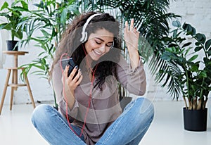 Young African American woman dressed casual listen to music and sitting on the floor at home