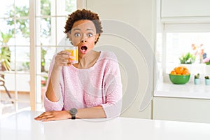 Young african american woman driking orange juice at home scared in shock with a surprise face, afraid and excited with fear