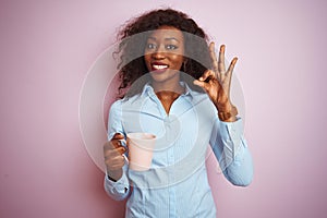 Young african american woman drinking cup of coffee over isolated pink background doing ok sign with fingers, excellent symbol