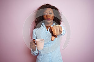 Young african american woman drinking cup of coffee over isolated pink background pointing with finger to the camera and to you,