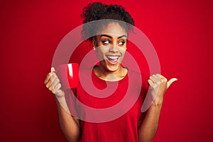 Young african american woman drinking a cup of coffee over isolated red background pointing and showing with thumb up to the side