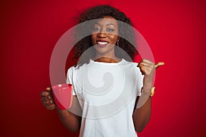 Young african american woman drinking cup of coffee over isolated red background pointing and showing with thumb up to the side