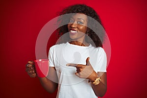 Young african american woman drinking cup of coffee over isolated red background very happy pointing with hand and finger