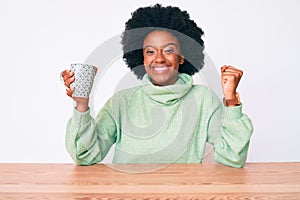 Young african american woman drinking cup of coffee screaming proud, celebrating victory and success very excited with raised arm