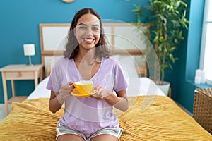 Young african american woman drinking cup of coffee sitting on bed at bedroom