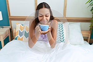 Young african american woman drinking cup of coffee sitting on bed at bedroom