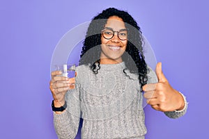 Young african american woman drinking glass of water over isolated purple background happy with big smile doing ok sign, thumb up