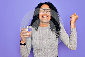 Young african american woman drinking glass of water over isolated purple background screaming proud and celebrating victory and