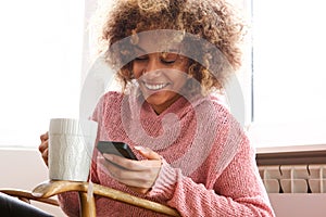 Young african american woman drinking hot cup of coffee and looking at cellphone photo