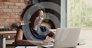 Young African American woman in earphones confer online using laptop