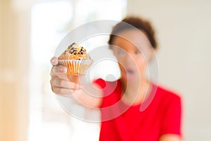 Young african american woman eating chocolate chips muffins scared in shock with a surprise face, afraid and excited with fear