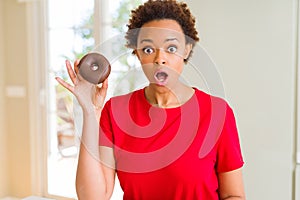 Young african american woman eating chocolate donut scared in shock with a surprise face, afraid and excited with fear expression