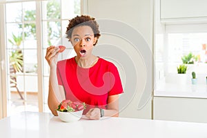 Young african american woman eating fresh strawberries for breakfast scared in shock with a surprise face, afraid and excited with