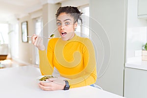 Young african american woman eating healthy green vegatables scared in shock with a surprise face, afraid and excited with fear