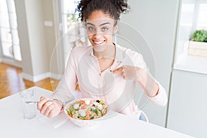 Young african american woman eating healthy pasta salad with surprise face pointing finger to himself