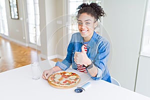 Young african american woman eating homemade mozzarella cheese pizza happy with big smile doing ok sign, thumb up with fingers,