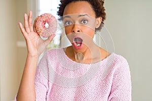 Young african american woman eating pink sugar donut scared in shock with a surprise face, afraid and excited with fear expression