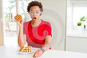 Young african american woman eating sweet waffle scared in shock with a surprise face, afraid and excited with fear expression