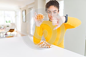 Young african american woman eating waffle belgiam pastry with angry face, negative sign showing dislike with thumbs down,