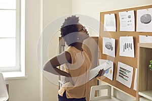 Young african american woman employee standing near board with graphs and charts