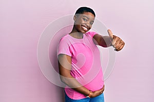 Young african american woman expecting a baby, touching pregnant belly approving doing positive gesture with hand, thumbs up