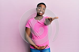 Young african american woman expecting a baby, touching pregnant belly smiling friendly offering handshake as greeting and