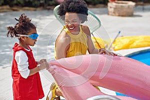 Young african american woman with her daughter by the pool with inflatable ring getting ready for summer activities