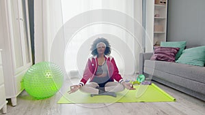Young african american woman hippy in colourful sportswear with curly afro hairs sits in lotus pose and meditations