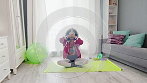 Young african american woman hippy in colourful sportswear with curly afro hairs sits in lotus pose and meditations