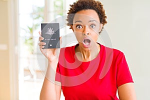 Young african american woman holding Australian passport scared in shock with a surprise face, afraid and excited with fear