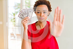 Young african american woman holding bank notes of fifty dollars with open hand doing stop sign with serious and confident