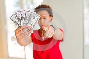 Young african american woman holding bank notes of fifty dollars pointing with finger to the camera and to you, hand sign,