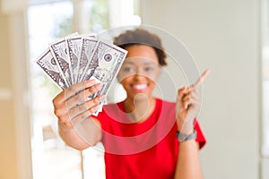 Young african american woman holding bank notes of fifty dollars very happy pointing with hand and finger to the side