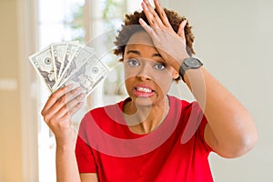 Young african american woman holding bank notes of twenty dollars stressed with hand on head, shocked with shame and surprise