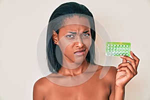 Young african american woman holding birth control pills clueless and confused expression