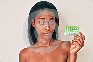 Young african american woman holding birth control pills relaxed with serious expression on face