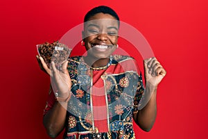 Young african american woman holding bowl of star anise screaming proud, celebrating victory and success very excited with raised