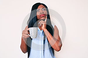 Young african american woman holding coffee serious face thinking about question with hand on chin, thoughtful about confusing