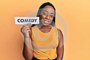 Young african american woman holding comedy word paper looking positive and happy standing and smiling with a confident smile