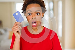 Young african american woman holding credit card scared in shock with a surprise face, afraid and excited with fear expression