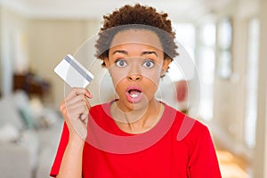 Young african american woman holding credit card scared in shock with a surprise face, afraid and excited with fear expression